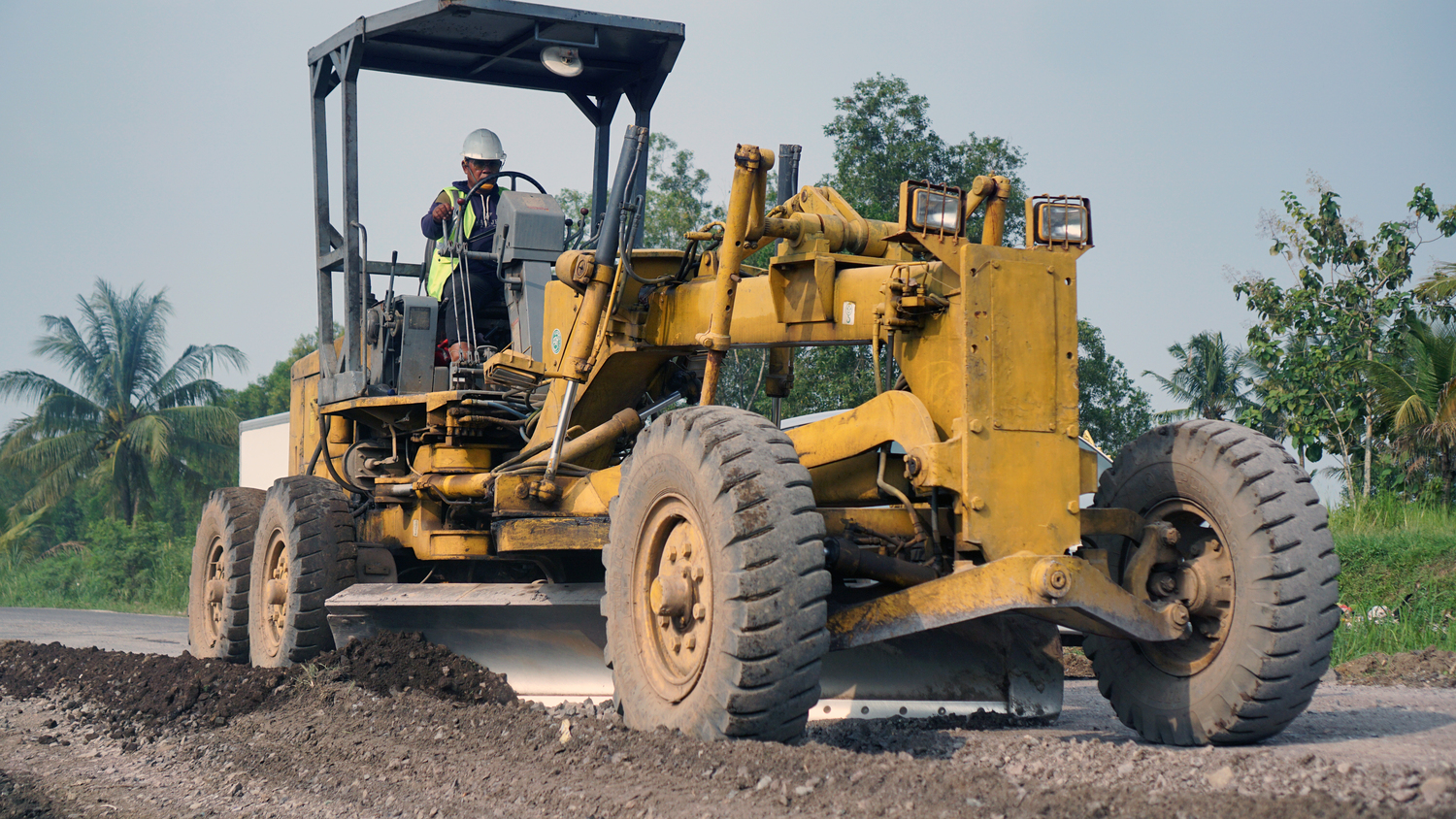a motor grader leveling stones and gravel for road repairs in Lampung. Front view.
